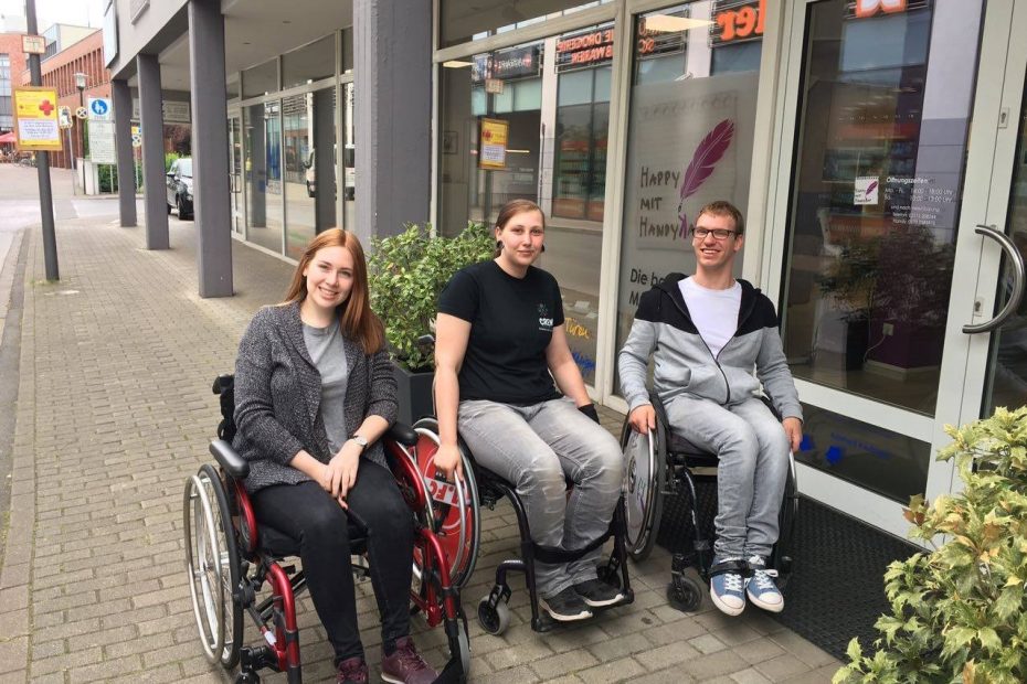 Drei Menschen im Rollstuhl draußen vor einem Geschäft