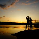 Die Silhouetten von zwei jungen Menschen vor einem Sonnenuntergang.